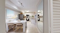 This well-appointed single-floor residence offers a cohesive, light-filled layout designed for comfortable everyday living. The heart of the home is an open-concept kitchen and dining area finished with large-format tile flooring that extends throughout the space. The kitchen is outfitted with white shaker-style cabinetry, granite-look countertops, and a full suite of stainless steel appliances, including a refrigerator, range, and over-the-range microwave. A central island adds additional workspace, while the adjacent dining area provides ample room for a full dining table and chairs. A full-length mirror near the entry enhances the sense of openness. The living room offers a warm, relaxed atmosphere with soft neutral tones, a ceiling beam accent, and sliding glass doors that allow natural light to fill the space. The bedrooms feature plush carpeting, large windows with outdoor views, and generous proportions suited for full-sized furnishings. The bathroom is finished with tile flooring and a walk-in shower. A dedicated in-unit laundry closet with a full-sized washer and dryer adds everyday convenience. Overall, the space presents a clean, modern aesthetic with a cohesive neutral palette throughout.