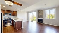 This well-appointed single-floor residence offers an open-concept living area filled with natural light and finished with rich hardwood flooring throughout. The spacious living room serves as the heart of the home, highlighted by a striking stone-tile fireplace surround that extends to the ceiling, adding both warmth and architectural character. Large sliding glass doors open to a private balcony with a metal railing, framing verdant treetop and hillside views that bring the outdoors in. Crown molding and a ceiling fan add refined touches to the living and entry areas. The kitchen is thoughtfully designed with rich dark-wood cabinetry, light quartz countertops, a peninsula with a double undermount sink, and a full suite of stainless steel appliances including a gas range, microwave, and dishwasher. Recessed lighting illuminates the kitchen, complementing the warm wood tones. The bedroom features mirrored sliding-door closets that maximize storage while enhancing the sense of space, along with crown molding and hardwood flooring consistent with the rest of the home. Additional doors lead to connecting spaces, ensuring a practical and connected floor plan. The overall ambiance is clean, modern, and inviting, with an emphasis on natural light and quality finishes throughout.