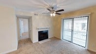 Located at 1030 Montlimar Dr in Mobile, Alabama, this single-story residence offers a comfortable and functional layout designed for everyday living. The living room serves as the heart of the home, centered around a classic white-mantled fireplace with a tiled hearth and glass doors, providing a warm focal point for the space. A ceiling fan with an integrated light fixture is mounted overhead, contributing to both comfort and ambiance. Wall-to-wall carpeting in a neutral tone runs throughout the living area, lending a soft, inviting feel underfoot. Natural light flows into the room through a full-length sliding glass door fitted with vertical blinds, offering easy access to the outdoors while allowing for adjustable light control. Crown molding and smooth wall finishes in warm, neutral tones give the interior a clean, well-maintained appearance. The open sightlines from the living area provide a clear view into the adjoining hallway, suggesting a straightforward and accessible floor plan. Overall, the space presents a tidy, move-in-ready environment with practical features suited for comfortable single-floor living in the Mobile, Alabama area.