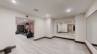 Located at 130 W Girard Ave in Philadelphia's vibrant Northern Liberties neighborhood, this fitness center offers a thoughtfully designed, two-zone workout facility spanning a generously sized single floor. The space is finished with light wood-look luxury vinyl plank flooring, neutral-toned walls, and recessed lighting throughout, creating a clean, modern aesthetic that feels both inviting and functional.

The cardio zone is the larger of the two areas and features multiple treadmills, elliptical machines, a stair climber, and a stationary bike, including an interactive cycling bike. A bold, contemporary mural with arched geometric shapes in warm terracotta and blush tones serves as a striking accent wall, adding visual energy to the space. A wall-mounted mirror at one end amplifies the sense of openness.

The strength training zone is a dedicated room equipped with a power rack, adjustable weight benches, a full set of dumbbells on tiered racks, and a cable machine. Floor-to-ceiling mirrors line two walls, allowing users to monitor their form effectively.

Adjacent to the main workout areas is a flexible open studio room featuring large wall mirrors, ideal for stretching, yoga, or group fitness activities. A water dispenser is conveniently located within the facility. Double glass entry doors with an accessible entrance complete this well-appointed fitness amenity.