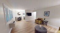 This 750 square foot suite at the Marin Suites Hotel offers a comfortable and well-appointed living space. The layout includes two bedrooms, a full bathroom, a living room, and a kitchen, all on a single floor. The primary bedroom is generously sized at 230 square feet, providing ample space for relaxation.

The living area features hardwood flooring throughout, creating a warm and inviting atmosphere. The room is furnished with a mustard-colored sofa and matching armchair, complemented by a round coffee table. Wall-mounted artwork adds a touch of sophistication to the space.

The bedrooms are equipped with comfortable beds, bedside tables, and additional furniture pieces such as dressers. Large windows with plantation shutters allow for natural light and temperature control. Wall-mounted TVs in both the living room and bedrooms provide entertainment options.

The kitchen, while compact, is fully functional with modern stainless steel appliances, including a refrigerator and coffee maker. White cabinetry and countertops keep the space bright and clean, with open shelving for additional storage.

The bathroom features a shower/tub combination with a curved shower rod, and a vanity with a granite countertop. The overall design of the suite is modern and minimalist, with a neutral color palette that creates a calming environment suitable for both short-term and extended stays.