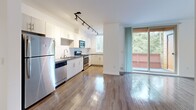 Located in Seattle's Greenwood neighborhood, this well-appointed 1-bedroom, 2-bathroom residence offers a thoughtfully designed single-floor layout that maximizes functionality and comfort. Wood-style flooring runs throughout the main living areas, lending a warm, cohesive aesthetic from room to room.

The heart of the home is an open-concept living, dining, and kitchen area bathed in natural light. The kitchen is outfitted with stainless steel appliances — including a refrigerator, range, microwave, and dishwasher — white cabinetry, and track lighting overhead. A sliding glass door connects this central space directly to a private balcony, offering pleasant outdoor views of surrounding greenery.

A long, well-lit hallway connects the living area to the private quarters, which include a generously sized bedroom with a dedicated closet, and a versatile den well-suited for a home office or additional sleeping space. Two full bathrooms provide added convenience, with tile flooring offering a clean contrast to the wood floors elsewhere. A dedicated in-unit laundry room with a full-size washer and dryer — complete with overhead wire shelving — rounds out the practical amenities of this move-in-ready Seattle residence.