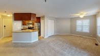 This single-floor residence offers a well-organized layout that balances open communal spaces with private quarters. The living area is generously proportioned, finished with neutral-toned carpet and warm taupe walls that create a calm, cohesive atmosphere. A ceiling fan overhead adds functional comfort, while a sliding glass door dressed with vertical blinds fills the space with natural light and provides outdoor access. A side window with horizontal blinds further brightens the room.

The kitchen is thoughtfully designed with rich, dark wood cabinetry extending to the ceiling for ample storage, granite-look countertops, and a full suite of stainless steel appliances including a range, over-the-range microwave, and refrigerator. A curved breakfast bar separates the kitchen from the adjacent living space, enhancing the open-concept feel. Adjacent to the kitchen is a double-door closet offering additional storage.

The bedroom is a well-sized, carpeted room with a large window providing natural light. It is complemented by a spacious walk-in closet outfitted with wire shelving systems for organized storage. The bathroom features a tub-shower combination with clean white tile surround, matching dark wood cabinetry, a white vanity, and neutral tile flooring, completing the unit with a polished, functional finish.