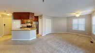 This single-floor residence offers a well-organized layout that balances open communal spaces with private quarters. The living area is generously proportioned, finished with neutral-toned carpet and warm taupe walls that create a calm, cohesive atmosphere. A ceiling fan overhead adds functional comfort, while a sliding glass door dressed with vertical blinds fills the space with natural light and provides outdoor access. A side window with horizontal blinds further brightens the room.

The kitchen is thoughtfully designed with rich, dark wood cabinetry extending to the ceiling for ample storage, granite-look countertops, and a full suite of stainless steel appliances including a range, over-the-range microwave, and refrigerator. A curved breakfast bar separates the kitchen from the adjacent living space, enhancing the open-concept feel. Adjacent to the kitchen is a double-door closet offering additional storage.

The bedroom is a well-sized, carpeted room with a large window providing natural light. It is complemented by a spacious walk-in closet outfitted with wire shelving systems for organized storage. The bathroom features a tub-shower combination with clean white tile surround, matching dark wood cabinetry, a white vanity, and neutral tile flooring, completing the unit with a polished, functional finish.