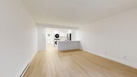 Located at Putnam Green in Greenwich, CT, this thoughtfully designed unit offers a clean, modern aesthetic throughout its single-floor layout. Light hardwood flooring runs continuously across the open-plan living, dining, and kitchen area, creating a cohesive and airy feel. White walls and recessed lighting enhance the brightness of the space, while a sliding glass door in the living area invites natural light and provides access to a greenery-filled outdoor view.

The kitchen is well-appointed with white shaker-style cabinetry, a white quartz peninsula that doubles as a dining counter, and a full suite of stainless steel appliances including a refrigerator, electric range, and over-the-range microwave. A stacked washer and dryer unit is conveniently integrated into the kitchen area, adding practical in-unit laundry without sacrificing the overall layout.

The full bathroom features a clean, all-white design with large-format subway tile surrounding a soaking tub and shower combination, a white vanity with chrome hardware, and light stone-tiled flooring. Baseboard heating is present throughout the unit. Three closets provide ample storage, keeping the living spaces open and uncluttered. The overall ambiance is bright, fresh, and move-in ready.