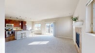 Located at 2212 New Port Vista Dr in Port Washington, Wisconsin, this well-appointed single-story home offers four bedrooms, two bathrooms, and a thoughtfully designed open-concept floor plan. The combined living, dining, and kitchen area forms the heart of the home, bathed in natural light streaming through large windows and a sliding glass door that opens to an outdoor balcony with neighborhood views. The living room is anchored by a tile-surround fireplace with a white mantel, adding warmth and character to the space, with soft carpeting underfoot throughout. The kitchen is a functional standout, featuring rich dark wood cabinetry, granite countertops, stainless steel appliances including a refrigerator, range, and built-in microwave, plus a peninsula with bar seating illuminated by stylish pendant lighting. Hardwood flooring runs through the kitchen and dining areas, creating a clean contrast to the carpeted living spaces. The primary bedroom provides a comfortable retreat with double-door closet access and natural light. Additional bedrooms are well-sized with neutral tones and ample natural light from dual windows. The bathrooms are finished with tile flooring, a sliding glass-door shower, and dark wood vanities with light stone countertops, completing this clean and move-in-ready home.