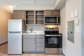 Located at 3841 E Washington Ave in Madison, Wisconsin, this studio unit offers a thoughtfully organized single-floor layout that maximizes every square foot. The open living area features light-toned hardwood-style flooring throughout, neutral-painted walls, and a textured ceiling with track lighting that provides flexible illumination. A large multi-pane window allows generous natural light to fill the space while offering outdoor views, and a wall-mounted HVAC unit ensures year-round climate control.

The kitchen is efficiently integrated into the unit and comes equipped with stainless steel appliances, including an electric range, microwave, and refrigerator, complemented by gray cabinetry with glass-front upper cabinets and a compact sink. A dedicated closet near the entry features a built-in hanging rod and overhead shelf, providing practical storage. The bathroom includes a full-width vanity mirror, an undermount sink with clean white countertops, and white tile detailing, conveying a simple, functional design. Overall, the unit presents a clean, modern aesthetic well-suited for efficient urban living in Madison's east side.