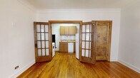 Located at 2350 N Cambridge Ave in Chicago's desirable Lincoln Park neighborhood, this single-floor unit blends vintage architectural charm with functional living spaces. Hardwood floors extend throughout, gleaming with warmth and adding a cohesive, classic aesthetic to every room.

The living area is generously proportioned, featuring crown molding, a ceiling fan with light fixture, and multiple windows framed in rich wood trim that allow natural light to fill the space. A cast-iron radiator adds to the unit's historic character. The entry door is a solid, heavy wood panel that reinforces the building's vintage appeal.

A standout architectural feature is the set of swinging French doors with multi-pane glass panels that separate the living area from the kitchen, offering both visual openness and the option for privacy. The kitchen is equipped with oak cabinetry, white subway tile backsplash, a gas range, dishwasher, and refrigerator. A cast-iron radiator and a solid wood back door are also present within the kitchen.

The bedroom receives abundant natural light through a large wood-trimmed window with views of surrounding greenery, and includes a ceiling fan overhead. The bathroom continues the vintage theme with classic penny-tile flooring, a full soaking tub with white tile surround, and a window for natural ventilation.