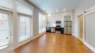 Located at 511 S Mangum St in the heart of Durham, NC, this single-floor unit offers a thoughtfully designed open-concept layout that seamlessly connects the living and kitchen areas. Warm hardwood flooring flows throughout the main living spaces, complemented by recessed lighting and large windows fitted with blinds that fill the interior with abundant natural light while offering views of the surrounding urban neighborhood.

The kitchen is a functional standout, featuring a two-tone cabinet design with crisp white upper cabinetry extending to the ceiling and dark lower cabinets for striking contrast. Stainless steel appliances — including a refrigerator, range, microwave, and dishwasher — are paired with clean white countertops and a built-in wine rack for added character. The space opens directly into the living area, making it ideal for everyday living and entertaining.

The bedroom is carpeted for comfort, offering a quiet retreat with neutral wall tones and ample room for furnishings. The bathroom is finished with white tile flooring, a glass-enclosed walk-in shower with mosaic tile detailing, a dark vanity with white countertop, and a full toilet. A walk-in closet with built-in shelving is conveniently accessible directly from the bathroom, adding practical storage to the space.