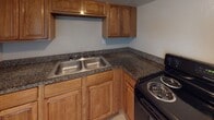 This single-floor space is designed with practicality and ease of living in mind. The layout, visible in the 3D floor plan, features an open flow between the living area and kitchen, connected by a wide doorway that promotes an accessible, cohesive feel throughout the unit.

The living area is finished with large, light-toned ceramic floor tiles that carry consistently throughout the entire space, lending a clean and unified aesthetic. Neutral beige walls complement the bright white baseboards and ceilings. A wall-mounted air conditioning unit and a large sliding window allow for natural light and ventilation. An additional room, similarly finished with tile flooring and a large window fitted with vertical blinds, provides versatile space suitable for a bedroom or secondary living area.

The kitchen is well-appointed with warm honey-toned wood cabinetry — both upper and lower — paired with dark granite-patterned countertops. A double-basin stainless steel sink sits beneath upper cabinets, and the kitchen includes a black electric range and refrigerator, offering all essential cooking amenities.

The bathroom features light tile flooring, a single-sink vanity with a large mirror, a wall-mounted light fixture, and a full bathtub with a tiled surround and shower combination, completing this straightforward and functional space.