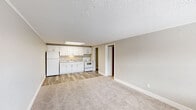 Located at 13809 Heron Wood Ln in Fort Myers, Florida, this single-floor unit offers a clean, functional layout designed for comfortable everyday living. The open-concept living area is finished with neutral-toned carpet and is bathed in a light, airy atmosphere accentuated by soft wall colors and white trim throughout. A textured ceiling adds a classic architectural detail consistent across the entire space.

The kitchen flows seamlessly from the living area and features updated white shaker-style cabinetry extending to the upper walls, providing generous storage. A light stone-finish countertop, single-basin stainless sink, white electric range, and a full-size white refrigerator complete the kitchen's practical setup. Wood-look plank flooring grounds the kitchen area and contrasts cleanly with the carpeted living spaces.

A hallway connects the living areas to the private rooms, including a well-appointed bathroom finished with wood-look flooring, a white vanity with matching cabinetry, a framed mirror, and a tub-shower combination. Additional rooms feature the same consistent neutral palette and carpeting, with windows allowing natural light to filter in. The entry door opens directly into the spacious main living area, offering a welcoming and open first impression.