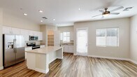 This well-appointed two-story home offers a clean, contemporary design throughout. The main level centers around an open-concept living and kitchen area, where wood-look plank flooring, recessed lighting, and ceiling fans create a bright and airy atmosphere. The kitchen is thoughtfully equipped with white shaker cabinetry, light quartz countertops, a central island, and a full suite of stainless steel appliances including a refrigerator with ice maker, electric range, and over-the-range microwave. A separate utility sink and open shelving pantry add practical functionality. The living and dining areas are bathed in natural light from multiple windows dressed with white blinds, with a glass-panel exterior door providing additional brightness and access to the outdoors. The bedrooms are finished with plush wall-to-wall carpet and ceiling fans, lending a comfortable, restful feel. The primary bedroom is complemented by an en-suite bathroom featuring wood-tone cabinetry, a quartz vanity, a glass-enclosed shower, and a dedicated walk-in closet. A dedicated laundry area houses a full-size washer and dryer. The staircase connects both floors seamlessly, completing this move-in-ready home.