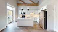 Located at 251 N Rose St in downtown Kalamazoo, MI, this 2-bedroom, 1-bathroom loft-style residence blends industrial character with modern finishes. The open-concept living, dining, and kitchen area is anchored by dramatic soaring ceilings with exposed wood beams and visible ductwork, lending authentic loft appeal. Light gray luxury vinyl plank flooring flows throughout, complementing the neutral palette.

The kitchen is a standout feature, boasting white shaker cabinetry, granite countertops, a subway tile backsplash, a central island with pendant lighting, and a full suite of stainless steel appliances including a range, microwave, dishwasher, and refrigerator. A striking exposed brick accent wall adds warmth and texture to the living area, which is bathed in natural light from large windows overlooking the surrounding neighborhood.

The spacious primary bedroom offers generous proportions with tall ceilings and ample natural light. Three closets provide excellent storage throughout the unit. The bathroom features a walk-in tiled shower with sliding glass doors, a white vanity with granite countertops, matte black hardware, and warm wood-tone flooring. Modern shaker-style interior doors with black hardware tie the design together, creating a cohesive, contemporary aesthetic throughout.