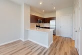 This 1-bedroom, 1-bathroom unit offers a thoughtfully organized layout across a single floor, making efficient use of its compact footprint. The open-concept living and kitchen area forms the heart of the unit, where light wood-style flooring and neutral walls create a clean, contemporary aesthetic. The kitchen is well-appointed with rich dark-wood cabinetry, white quartz countertops, and a full suite of stainless steel appliances including a refrigerator, range, microwave, and dishwasher. A peninsula with an undermount sink provides additional prep space and serves as a natural divider between the kitchen and living area. The living room benefits from multiple windows dressed with horizontal blinds, allowing generous natural light to filter in alongside views of surrounding greenery, including palm trees. A ceiling fan adds comfort to the space. The bedroom is a comfortable size, featuring plush carpet flooring, a ceiling fan, and a large window with outdoor views that bring in ample natural light. The bathroom is finished with a dark-wood vanity, white countertop, a large mirror, and a shower-tub combination. A hallway connects the main living spaces, completing this efficiently designed unit.