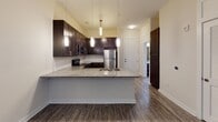 This well-appointed single-floor residence offers a thoughtfully designed open-concept layout that seamlessly connects the kitchen and living area. The kitchen serves as the centerpiece of the space, showcasing rich dark-espresso cabinetry, granite countertops, and a full suite of stainless steel appliances including an electric range, microwave, dishwasher, and refrigerator. A classic white subway tile backsplash adds a clean, contemporary contrast, while pendant lighting and a track light system overhead provide both task and ambient illumination. The peninsula-style island offers additional counter space and sink access, making it ideal for both cooking and casual dining.

Wood-look flooring flows consistently throughout the unit, lending warmth and cohesion to the open living area, which is finished with a ceiling fan and direct access to a private balcony with views of the surrounding building exterior. A dedicated bedroom features multiple windows that bring in natural light, complemented by neutral wall tones and the same wood-look flooring. The bathroom is finished with grey tile surrounding a soaking tub and shower combination, a granite vanity, and wood-look tile flooring. A stacked in-unit washer and dryer completes this practical and modern living space.