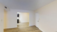 This single-story unit offers three bedrooms and two bathrooms within a thoughtfully arranged floor plan. The living area features wood-style plank flooring and neutral white walls that create a clean, bright atmosphere. A textured popcorn ceiling adds a classic touch overhead. An open archway connects the living space to the kitchen, which is visible from the main area and showcases dark cabinetry contrasted against light countertops, providing a modern aesthetic. The entry door opens directly into the living space, offering a straightforward and functional layout. The consistent flooring throughout the main areas ties the spaces together cohesively. The overall design emphasizes simplicity and practicality, with a neutral color palette that allows for versatile interior styling. The unit's single-floor layout ensures easy accessibility between all rooms, making it a functional and comfortable space suited for a range of lifestyles.