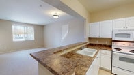 Located in the Porter Ranch neighborhood of Los Angeles, this single-floor unit offers a practical and comfortable layout suited for everyday living. The kitchen is equipped with white cabinetry, dark granite-style countertops, tile flooring, and a full suite of white appliances including a refrigerator, electric range, microwave, and dishwasher. A peninsula with a double basin sink extends into the living area, creating an open, connected feel between the kitchen and the main living space.

The living area is generously sized with soft carpeting and neutral warm-toned walls that carry throughout the unit. Large windows and a sliding glass door fitted with vertical blinds allow natural light to fill the room while providing access to a private balcony with outdoor views. The open floor plan creates a seamless transition between the living and dining areas, making the space feel airy and functional.

The bedroom is well-proportioned with carpeted floors, ample closet storage, and direct access to the bathroom. The bathroom features tile flooring, a white vanity with dual mirrors, and a clean, bright finish. The unit's consistent use of neutral tones, white trim, and practical finishes throughout creates a cohesive and move-in-ready environment.