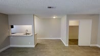 This single-floor unit offers a thoughtfully designed open layout that maximizes functionality and livability. The main living area is finished with warm wood-look plank flooring that extends throughout, complemented by neutral gray-toned walls and crisp white baseboards that create a clean, modern aesthetic.

A half-wall pass-through separates the kitchen from the living space, featuring a double basin sink set into a light-colored countertop — an ideal detail that maintains an open, connected feel between the two areas. The textured popcorn ceiling adds a classic touch overhead, while flush-mount ceiling lighting provides consistent illumination across the space.

Ceiling-mounted HVAC vents ensure efficient climate control throughout the unit. Adjacent to the main living area, a doorway leads to an additional space that reveals a generously sized walk-in closet, offering ample storage capacity with visible shelving.

The overall ambiance of the space is bright, neutral, and move-in ready, with a straightforward and practical design that accommodates a variety of furnishing arrangements. The open floor plan, cohesive finishes, and well-placed architectural details make this a versatile and comfortable single-level living space.