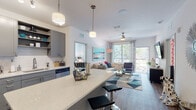 This single-story residence is thoughtfully designed with a modern, open-concept layout that seamlessly connects the kitchen, dining, and living areas. The kitchen is a standout feature, outfitted with grey shaker-style cabinetry, open shelving, a white quartz countertop island with bar seating, a full suite of stainless steel appliances, and a white subway tile backsplash. Wood-look flooring runs throughout the main living areas, adding warmth to the contemporary aesthetic.

The living room is bright and welcoming, benefiting from large windows and a sliding glass door that opens to a balcony with outdoor views. A ceiling fan overhead adds both function and style. The space accommodates comfortable seating and a media area with ease.

The two bedrooms are well-proportioned, each featuring large windows that invite natural light and offer views of the surrounding greenery. Both rooms include wood-look flooring and ample space for storage.

The two bathrooms are finished with the same grey cabinetry and white quartz vanities found throughout the residence. One bathroom features a tub-shower combination with tile surround, while the other includes a shower with a bold chevron-patterned curtain. Marble-look tile flooring completes each bathroom's clean, polished look.