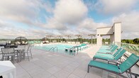 Located along Big Bend Road in Twin Oaks, Missouri, this rooftop pool and amenity deck offers a well-appointed outdoor retreat designed for both relaxation and social gathering. The centerpiece of the space is a generously sized swimming pool with crystal-clear water, built-in entry steps, and multiple access points via stainless steel railings. The surrounding deck is finished in large-format light gray porcelain tile, providing a clean, modern aesthetic underfoot.

Rows of teal-cushioned lounge chairs line the perimeter of the deck, offering ample space for sunbathing with open sky above. A glass railing system runs along the outer edges of the rooftop, ensuring unobstructed panoramic views of the Twin Oaks landscape while maintaining a secure boundary. Several pergola structures with string lighting provide shaded dining and seating areas, furnished with white tables and chairs suited for casual outdoor meals or conversation.

A distinctive hanging egg chair adds a stylish lounge nook near the pool's edge. The space is accessed through a glass-panel door set within a modern tile-clad exterior wall. The overall design is contemporary and cohesive, combining functional amenities with elevated outdoor living in an open-air rooftop setting.
