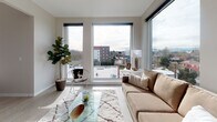 This thoughtfully designed single-floor residence offers a seamless blend of modern aesthetics and functional living. The open-concept living area is a standout feature, anchored by expansive floor-to-ceiling windows on multiple walls that flood the space with natural light and frame sweeping panoramic views of the surrounding cityscape and distant mountains. Light hardwood-style flooring runs throughout, complementing the neutral, warm tones of the interior palette.

The kitchen is outfitted with flat-front wood-grain cabinetry extending to the ceiling, stainless steel appliances including a gas range with over-range microwave, and a clean quartz countertop with an undermount sink. The layout connects effortlessly to the living area, making it ideal for everyday living and entertaining.

The bedroom is a calm, restful retreat finished in soft grey tones, featuring louvered closet doors and warm accent artwork above the bed, creating a cozy and inviting atmosphere.

The bathroom maintains the home's contemporary design language with wood-tone cabinetry, a white quartz vanity top, tile-look flooring, and brushed nickel fixtures. A framed art piece adds a touch of personality to the space.

Overall, this residence offers a refined, light-filled living experience with modern finishes and impressive outdoor views throughout.