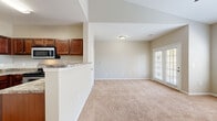 This well-appointed 2-bedroom, 1-bathroom single-floor residence offers a practical and comfortable layout across a compact yet efficiently designed floor plan. The open-concept living and kitchen area serves as the heart of the home, where the kitchen transitions seamlessly into the carpeted living room. The kitchen is equipped with rich, warm-toned wood cabinetry, granite-look countertops, stainless steel appliances including an over-the-range microwave and electric range, and durable hardwood flooring. The living room is bright and airy, benefiting from large windows with blinds and a set of French doors that invite natural light and outdoor views. A ceiling fan adds comfort overhead.

The spacious primary bedroom features vaulted ceilings, a ceiling fan, plush wall-to-wall carpeting, and generous window coverage that fills the room with natural light. It is complemented by a dedicated walk-in closet outfitted with wire shelving for organized storage. The second bedroom is cozy and carpeted, offering a versatile space suitable for guests or a home office. The full bathroom includes a tub-shower combination with white tile surround, a toilet, dark wood cabinetry for storage, and neutral tile flooring, completing this functional and inviting residence.
