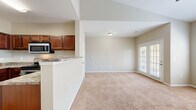This well-appointed 2-bedroom, 1-bathroom single-floor residence offers a practical and comfortable layout across a compact yet efficiently designed floor plan. The open-concept living and kitchen area serves as the heart of the home, where the kitchen transitions seamlessly into the carpeted living room. The kitchen is equipped with rich, warm-toned wood cabinetry, granite-look countertops, stainless steel appliances including an over-the-range microwave and electric range, and durable hardwood flooring. The living room is bright and airy, benefiting from large windows with blinds and a set of French doors that invite natural light and outdoor views. A ceiling fan adds comfort overhead.

The spacious primary bedroom features vaulted ceilings, a ceiling fan, plush wall-to-wall carpeting, and generous window coverage that fills the room with natural light. It is complemented by a dedicated walk-in closet outfitted with wire shelving for organized storage. The second bedroom is cozy and carpeted, offering a versatile space suitable for guests or a home office. The full bathroom includes a tub-shower combination with white tile surround, a toilet, dark wood cabinetry for storage, and neutral tile flooring, completing this functional and inviting residence.