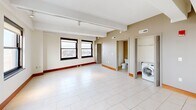 Located in the heart of downtown Detroit, this two-bedroom, two-bathroom residence offers a well-appointed urban living experience across a single thoughtfully designed floor. The open-concept layout seamlessly connects the living, dining, and kitchen areas, all finished with large-format white tile flooring and bathed in natural light from an array of black-framed windows that frame striking city views, including a notable overlook of a major Detroit landmark stadium.

The kitchen is a standout feature, equipped with warm wood cabinetry, stainless steel appliances including a side-by-side refrigerator, electric range, and built-in microwave, complemented by a granite-topped island and a textured stone tile backsplash. Track lighting and recessed fixtures illuminate the space effectively.

Both bedrooms are carpeted and offer a calm, neutral palette. The primary bedroom benefits from floor-to-ceiling windows with expansive city views and direct access to a well-appointed en-suite bathroom featuring a granite-surround soaking tub, a separate glass-enclosed shower, and a dark-vanity with an integrated sink. A second full bathroom and dedicated laundry area with an in-unit washer add further convenience. Each bedroom is paired with its own closet.