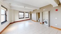 Located in the heart of downtown Detroit, this two-bedroom, two-bathroom residence offers a well-appointed urban living experience across a single thoughtfully designed floor. The open-concept layout seamlessly connects the living, dining, and kitchen areas, all finished with large-format white tile flooring and bathed in natural light from an array of black-framed windows that frame striking city views, including a notable overlook of a major Detroit landmark stadium.

The kitchen is a standout feature, equipped with warm wood cabinetry, stainless steel appliances including a side-by-side refrigerator, electric range, and built-in microwave, complemented by a granite-topped island and a textured stone tile backsplash. Track lighting and recessed fixtures illuminate the space effectively.

Both bedrooms are carpeted and offer a calm, neutral palette. The primary bedroom benefits from floor-to-ceiling windows with expansive city views and direct access to a well-appointed en-suite bathroom featuring a granite-surround soaking tub, a separate glass-enclosed shower, and a dark-vanity with an integrated sink. A second full bathroom and dedicated laundry area with an in-unit washer add further convenience. Each bedroom is paired with its own closet.
