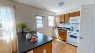 This 3-bedroom, 2-bathroom residence is thoughtfully laid out across two floors, offering a comfortable and functional living environment. The kitchen is a standout feature, showcasing rich dark granite countertops that contrast beautifully with warm honey-toned hardwood flooring. Honey-stained wood cabinetry provides ample storage, while white appliances — including a gas range, dishwasher, and built-in microwave — lend a clean, classic look. A central kitchen island with matching granite offers additional prep space and casual seating. Natural light pours in through multiple windows, brightening the space and creating an inviting atmosphere. A door off the kitchen provides convenient exterior access. The two-story layout allows for a natural separation between living and sleeping areas, adding to the home's sense of privacy and organization. Neutral wall tones throughout complement the warm wood finishes, creating a cohesive and welcoming ambiance. With three well-sized bedrooms and two full bathrooms, this home provides ample space for comfortable everyday living.