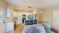 Located at 1111 Elk Knob Trl in Fayetteville, NC, this well-appointed two-story home offers three bedrooms, four bathrooms, and a thoughtful layout spread across two floors. The main level hosts an open-concept kitchen and living area finished with light hardwood-style flooring throughout. The kitchen is a standout feature, showcasing crisp white shaker cabinetry, a marble-top island with seating for multiple bar stools, stainless steel appliances including a French door refrigerator and over-the-range microwave, and stylish pendant lighting. The living area flows naturally from the kitchen, offering multiple windows that bring in natural light, a ceiling fan, and a warm, neutral color palette. Wainscoting details add a refined touch to the hallways. The upper floor hosts the bedrooms, each carpeted and equipped with ceiling fans. The primary bedroom offers a generous footprint with its own closet access. Secondary bedrooms include closets and share well-placed bathrooms. A dedicated laundry room with wire shelving and washer/dryer hookups adds everyday convenience. The attached garage provides secure parking and additional storage space. Throughout the home, clean finishes, recessed lighting, and neutral tones create a bright, move-in-ready atmosphere.