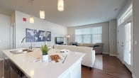Located at 8432 S 27th St in Oak Creek, Wisconsin, this single-floor residence offers a thoughtfully designed open-concept layout that seamlessly connects the kitchen, dining, and living areas. The kitchen is a standout feature, showcasing rich dark wood cabinetry, stainless steel appliances, and a large center island with a bright white quartz countertop and bar seating — ideal for both cooking and casual dining. Pendant lighting adds a stylish touch overhead. Adjacent to the kitchen, the dining area benefits from a large window that fills the space with natural light and provides views of the surrounding neighborhood. The open living room is warm and inviting, with rich hardwood-style flooring, neutral-toned walls, and generous windows dressed with horizontal blinds that allow for abundant natural light. The bedroom is generously proportioned, featuring plush carpeting, a natural light-filled window, and direct access to a walk-in closet with built-in shelving. The bathroom continues the refined aesthetic with hardwood-style flooring, a dark wood vanity with a white countertop, and access to an additional walk-in closet. Throughout the residence, a consistent palette of neutral tones, modern finishes, and practical design choices create a comfortable and contemporary living environment.