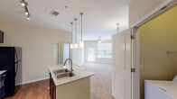 This single-story, one-bedroom, one-bathroom unit offers a thoughtfully designed open-concept layout with distinct zones for living, dining, and cooking. The kitchen serves as a focal point, showcasing rich dark cabinetry that extends to the ceiling, granite countertops, black appliances including a range, microwave, and refrigerator, and a kitchen island with a double stainless-steel sink beneath stylish pendant lighting. Track lighting and wood-style flooring complete the kitchen's polished look. A dedicated laundry area with a full-size washer and dryer is conveniently tucked just off the kitchen. The living area features plush carpeting, a ceiling fan, and large windows with blinds that admit generous natural light, along with access to an outdoor space. The bedroom is a comfortable retreat with soft carpet, a ceiling fan, ample natural light from a sizable window, and a walk-in closet with built-in rod storage. The bathroom includes a soaking tub with a tiled surround, a shower, toilet, and wood-style flooring. Neutral wall tones throughout create a cohesive, welcoming ambiance.