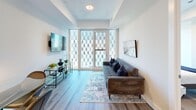 This thoughtfully designed one-bedroom, one-bathroom unit offers a efficient and modern layout across a single floor. Light wood-tone flooring runs throughout, creating a cohesive and contemporary aesthetic.

The open-concept living and kitchen area is the heart of the unit. The kitchen features white cabinetry, a clean white countertop with an undermount sink, and a full suite of stainless steel appliances, including a refrigerator, dishwasher, electric range, and over-the-range microwave. A subway tile backsplash adds a polished finishing touch. A peninsula counter separates the kitchen from the living area, providing additional prep space and a natural transition between zones.

The living room is bright and welcoming, anchored by large floor-to-ceiling windows that allow ample natural light and offer views of the surrounding urban architecture. The space comfortably accommodates a full sofa and media setup, with track lighting overhead.

The bedroom is a quiet retreat, also featuring floor-to-ceiling windows with urban views. The bathroom is clean and modern, finished in white tile with a glass-enclosed walk-in shower and a stacked in-unit washer and dryer conveniently integrated into the space.

A keypad-secured entry door and a small nook near the entrance provide functional workspace potential, completing this well-appointed unit.