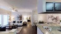 This single-story residence showcases an open-concept floor plan that integrates the kitchen, dining, and living areas into one cohesive, flowing space. Rich dark hardwood flooring extends throughout the main living area, providing a warm contrast to the light-toned walls and textured ceilings. The living room is anchored by a ceiling fan and features crown molding, lending a polished, finished look. A comfortable seating arrangement with a sofa accented by navy and neutral throw pillows sits beneath a contemporary piece of wall art, completing the inviting atmosphere.

The kitchen is positioned prominently within the open layout and features granite countertops with a raised breakfast bar, offering both additional prep space and casual seating. A large range hood serves as a functional focal point above the cooking area. Adjacent to the kitchen, the dining area provides space for a full table setup. A hallway visible from the main living space leads to additional rooms, including what appears to be a bedroom with a louvered closet door, maintaining a sense of privacy while preserving the open flow of the home.