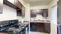 This single-floor residence offers a thoughtfully designed layout with a range of functional spaces. The kitchen is equipped with rich dark-stained cabinetry offering ample upper and lower storage, granite-style countertops, a black appliance suite including an electric range, dishwasher, and full-size refrigerator, and light wood-look flooring that adds a clean, modern touch. A window allows natural light to brighten the workspace, complementing the practical and organized design.

The living area is generously sized, featuring plush gray carpeting and a distinctive slate-blue accent wall that adds depth and character to the room. Natural light filters in through a large window, and a hallway connects the space to the rest of the home.

The bedrooms are comfortable and well-proportioned, each finished with warm neutral-toned carpet and windows fitted with blinds for light control and privacy. Closets with shelving provide practical storage solutions in the sleeping areas.

The bathroom is finished with warm beige tile work on the walls, a light wood vanity with a white basin sink, and a shower/tub combination accented by a marble-patterned curtain. A window with vertical blinds brings in natural light, creating a bright and clean atmosphere throughout.