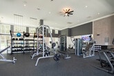 This fitness center in Huntsville, Alabama, is designed to accommodate a wide range of workout styles within a thoughtfully organized, single-level space. The facility is divided into distinct functional zones, each outfitted to support different training needs.

The strength training area features a comprehensive selection of weight machines, cable systems, free weights, and adjustable benches arranged across durable rubber flooring. Ceiling fans and recessed lighting provide a well-lit, comfortable environment, while large mirrors along the walls enhance the sense of space and allow for form monitoring. Mounted flat-screen televisions are positioned throughout this zone.

A separate functional training area transitions to light wood-style flooring and benefits from soaring double-height ceilings and an expansive bank of large windows that allow generous natural light and views of the surrounding greenery. This area includes stability balls, balance equipment, and an Echelon connected fitness display. Open shelving provides organized storage for accessories.

A dedicated heavy training room features dark accent walls, a full garage-style glass door that opens to outdoor views, and houses a power rack, barbells, weight plates, kettlebells, and treadmills on rubberized flooring. Near the entrance, a water station and large display screen complete the amenities of this modern, fully appointed fitness facility.