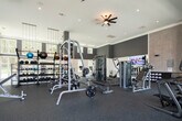 This fitness center in Huntsville, Alabama, is designed to accommodate a wide range of workout styles within a thoughtfully organized, single-level space. The facility is divided into distinct functional zones, each outfitted to support different training needs.

The strength training area features a comprehensive selection of weight machines, cable systems, free weights, and adjustable benches arranged across durable rubber flooring. Ceiling fans and recessed lighting provide a well-lit, comfortable environment, while large mirrors along the walls enhance the sense of space and allow for form monitoring. Mounted flat-screen televisions are positioned throughout this zone.

A separate functional training area transitions to light wood-style flooring and benefits from soaring double-height ceilings and an expansive bank of large windows that allow generous natural light and views of the surrounding greenery. This area includes stability balls, balance equipment, and an Echelon connected fitness display. Open shelving provides organized storage for accessories.

A dedicated heavy training room features dark accent walls, a full garage-style glass door that opens to outdoor views, and houses a power rack, barbells, weight plates, kettlebells, and treadmills on rubberized flooring. Near the entrance, a water station and large display screen complete the amenities of this modern, fully appointed fitness facility.