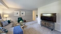 This thoughtfully designed 2-bedroom, 1-bathroom residence at Governor Sproul Apartments in Broomall, PA offers a comfortable and modern living experience across a single floor. The layout flows naturally from a spacious combined living and dining area into a separate formal dining space, providing versatile options for everyday living and entertaining. The living room features plush carpeting, neutral grey walls, and ample space for relaxed seating arrangements. The dedicated dining area is anchored by a pendant light fixture and a sliding glass door that opens to views of the lush, tree-lined grounds. The kitchen is fully updated with crisp white shaker cabinetry, light granite-style countertops, stainless steel appliances including a range, microwave, and dishwasher, and durable wood-look flooring. Both bedrooms are carpeted and receive natural light through large windows that frame peaceful outdoor greenery. The primary bedroom offers generous proportions and views of the surrounding landscape. The bathroom is clean and classic, featuring a white vanity with a brushed gold faucet and a mirrored medicine cabinet. Throughout the residence, a cohesive neutral palette and quality finishes create a calm, welcoming ambiance complemented by the community's expansive green outdoor surroundings.