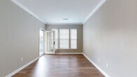 This single-floor residence is designed with a neutral, cohesive aesthetic throughout, featuring warm greige walls, crisp white trim, and consistent wood-style flooring across the main living areas. The open living and dining area benefits from natural light streaming through a trio of windows with blinds, and a glass-paned door that leads to an outdoor balcony, enhancing the sense of openness.

The kitchen is equipped with stainless steel appliances, including a gas range, over-the-range microwave, and refrigerator. White shaker-style cabinetry and a classic white subway tile backsplash complete the space, which connects seamlessly to the main living area via a pass-through counter.

A hallway lined with white trim leads to the bedrooms, each finished with plush carpeting and generous natural light. The primary bedroom includes a spacious walk-in closet outfitted with wire shelving on both sides for organized storage.

The bathroom features a full tub and shower combination with white tile surround accented by a decorative tile border, a white vanity, and wood-style flooring, finished with matte black hardware throughout for a modern touch.