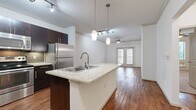This single-story, one-bedroom, one-bathroom unit is thoughtfully designed to maximize its compact footprint. The open-concept layout connects the kitchen and living area seamlessly, creating an efficient and functional living space. Crown molding runs throughout, adding a refined architectural detail to the interior.

The kitchen is a standout feature, equipped with dark espresso cabinetry, a mosaic tile backsplash, stainless steel appliances including a range, microwave, and refrigerator, and a central island topped with light granite countertops. Pendant lighting and a track lighting system illuminate the space effectively. The kitchen flows directly into the living area, which features warm hardwood flooring, a ceiling fan, and French doors that introduce natural light and outdoor views.

The bedroom offers plush carpeting, a ceiling fan, crown molding, and windows with outdoor views, providing a comfortable and quiet retreat. A dedicated closet adds practical storage. The hallway connects the main living areas to the bedroom and bathroom.

The bathroom is finished with large-format tile flooring, a dark vanity with granite countertop, and a full soaking tub surrounded by neutral ceramic tile. The overall ambiance of the unit is modern and cohesive, with consistent finishes throughout.