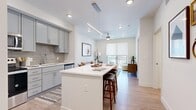 Located at 5 Tree Farm Drive in Carbondale, Colorado, this thoughtfully designed one-bedroom, one-bathroom residence offers a clean, modern aesthetic throughout its efficiently arranged single-floor layout. The open-concept kitchen and living area serves as the heart of the home, anchored by a sleek kitchen featuring gray shaker-style cabinetry extending to the ceiling, a subway tile backsplash, white quartz countertops, a large central island with bar seating, and a full suite of stainless steel appliances including a refrigerator, range, microwave, and dishwasher. Light wood-style flooring flows throughout the main living areas, complementing the bright, neutral palette. The living room is bathed in natural light from a sliding glass door that opens onto a private balcony, offering outdoor seating and views of the surrounding greenery. A ceiling fan adds comfort to both the living room and bedroom. The carpeted bedroom provides a quiet retreat with large windows, ample natural light, and access to a spacious walk-in closet with built-in shelving. The bathroom is finished with light wood-style flooring, gray cabinetry with a white countertop vanity, and a glass-enclosed walk-in shower. The overall ambiance is contemporary and cohesive, with a clean, move-in-ready feel.
