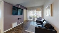 This single-floor residence in Gainesville, Florida offers a functional and comfortable layout designed for everyday living. The open-concept living area features wood-look flooring, a textured ceiling, and a sliding glass door that fills the space with natural light and provides access to a private balcony with outdoor views. A bold accent wall adds a pop of color, complementing the sleek leather seating and wall-mounted television.

The kitchen is efficiently designed with white cabinetry, dark countertops, and stainless steel appliances including a range, over-the-range microwave, and refrigerator. A breakfast bar with seating connects the kitchen to the main living space. Adjacent to the kitchen, a dedicated dining area accommodates a full-sized table and chairs beneath a ceiling fan.

The bedrooms are carpeted for comfort and include ceiling fans, window blinds for privacy, and mirrored sliding closet doors that maximize perceived space. The bathroom is clean and bright, featuring a white vanity with under-sink storage, a tub/shower combination, and wood-look flooring.

A dedicated utility room houses a full-size washer and dryer alongside the water heater, offering added convenience within the residence. Throughout, the layout is practical and cohesive.