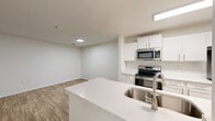 Located at Cameron Woods in Apex, NC, this one-bedroom, one-bathroom residence offers a thoughtfully designed single-floor layout that maximizes every square foot. The open-concept living area seamlessly connects the kitchen, dining, and living spaces, all finished with warm wood-look flooring and neutral walls that create a bright, clean aesthetic. A ceiling fan with a window overlooking the outdoors adds comfort and natural light to the living room.

The kitchen is a standout feature, showcasing crisp white shaker cabinetry, a classic subway tile backsplash, stainless steel appliances including a range and built-in microwave, and a spacious peninsula with a quartz countertop and undermount sink — ideal for both cooking and casual dining. A dedicated pantry provides additional storage.

The bedroom is carpeted for comfort and benefits from a large window that allows ample natural light to filter in. It includes access to a walk-in closet with built-in shelving. The full bathroom features a clean, all-white tub-shower combination with brushed nickel fixtures.

Practical amenities include an in-unit laundry area and a utility room. The entrance hallway offers a welcoming transition into the home with an adjacent closet. The overall design is modern, functional, and move-in ready.