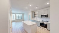 Located on W Mallard Creek Church Rd in Charlotte, NC, this well-appointed 2-bedroom, 2-bathroom residence offers a thoughtfully designed single-floor layout with a clean, modern aesthetic throughout. Light wood-tone flooring runs continuously through the living spaces, creating a warm and cohesive feel.

The kitchen is a standout feature, showcasing sleek gray cabinetry, stainless steel appliances including a French door refrigerator and range, recessed lighting, and a generous central island with a crisp white countertop — ideal for both meal prep and casual dining. The adjacent living room and dining area are filled with natural light, with a sliding glass door opening onto a private balcony that overlooks a landscaped courtyard and the surrounding community.

Both bedrooms are comfortably sized, each featuring large windows with blinds, ceiling fans, and light-filled interiors. The primary bedroom includes an en-suite bathroom with a wide vanity, white quartz countertop, gray cabinetry, and a large framed mirror. Each bedroom is accompanied by a dedicated walk-in closet equipped with wire shelving systems for organized storage.

The second bathroom mirrors the refined finishes found throughout the home. The overall design emphasizes neutral tones, modern fixtures, and functional layouts, making this a bright and inviting Charlotte residence.