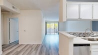 Located at 11657 Oxnard St in North Hollywood, CA, this well-appointed 2-bedroom, 2-bathroom unit offers a thoughtfully designed single-level layout. Light gray wood-look flooring runs throughout, complementing the bright, neutral palette that gives each room an open, airy feel.

The combined kitchen and living area forms the heart of the home. The kitchen features white cabinetry, a mosaic tile backsplash, light countertops with a peninsula, stainless steel appliances, and a built-in sink. It opens seamlessly into a spacious living room illuminated by natural light pouring through a full-width sliding glass door that leads to a private balcony. The balcony overlooks a lushly landscaped courtyard with tropical palms, banana trees, and a pool — a serene Southern California outdoor retreat.

The primary bedroom is generously sized with a sliding door that also connects to outdoor space, and the unit includes three closets in total, one of which is a well-organized walk-in closet outfitted with built-in shelving and hanging rods. Both bathrooms are finished with elegant marble-style tile surround in the tub/shower areas, white vanities, and matching light flooring. Textured ceilings complete the classic character of this clean, move-in-ready North Hollywood residence.