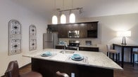 Located at 6634 Riverside Drive in Dublin, Ohio, this single-story space showcases a well-appointed kitchen as a central highlight. The kitchen is designed with rich, dark espresso-toned cabinetry that extends to the upper walls, providing generous storage throughout. A large granite-topped island serves as the focal point, offering seating for casual dining and an integrated sink for added convenience. Three pendant lights hang above the island in a linear track configuration, casting warm, focused illumination over the workspace.

Stainless steel appliances, including a refrigerator, microwave, and range, complement the dark cabinetry and contribute to the kitchen's cohesive, modern aesthetic. The light-toned granite countertops provide a striking contrast against the darker elements, creating a balanced and visually appealing design. A built-in wine rack adds a refined touch to the upper cabinetry. The overall ambiance of the kitchen is polished and functional, blending contemporary finishes with practical design elements suited for everyday living and entertaining.