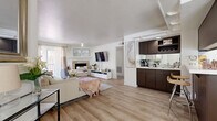 Located in Mesa, Arizona, this single-floor, 2-bedroom, 3-bathroom residence offers a thoughtfully designed open-concept layout that maximizes every square foot. Light wood-style flooring flows through the main living areas, creating a bright and cohesive aesthetic. The living room is inviting and spacious, anchored by a tiled fireplace and large windows that invite natural light, while a cozy dining nook with a glass-top table sits adjacent, offering outdoor views through slatted blinds. The kitchen is a standout feature, boasting dark espresso cabinetry, a central island with a dramatic range hood, a breakfast bar, and black appliances — all topped by a distinctive coffered ceiling detail. The primary bedroom includes plush carpeting, access to natural light via vertical blinds, and an en-suite bathroom featuring a dual-sink dark vanity with mirrored sliding closet doors. The second bedroom offers comfortable carpeted space, ample natural light, and its own closet. A full bathroom with a shower-tub combo serves guests. The dedicated laundry room includes a full-size washer and dryer with open shelving. This home combines practical function with clean, modern style in a convenient Mesa location.