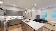 This well-designed single-floor residence showcases a cohesive modern aesthetic with clean lines, neutral tones, and quality finishes throughout. The heart of the home is an expansive open-concept kitchen that flows seamlessly into the living area. The kitchen is outfitted with grey shaker-style cabinetry, crisp white quartz countertops, a white subway tile backsplash, and a full suite of stainless steel appliances. A central island with an undermount sink and pendant lighting above serves as both a functional workspace and a casual gathering point. Light hardwood flooring runs throughout the main living areas, adding warmth to the contemporary palette. The living space features large windows that invite natural light and create an airy, comfortable atmosphere. The primary bedroom offers a striking four-poster bed frame, a window with natural light, and direct access to an en-suite bathroom. The primary bath is equipped with a dual-sink vanity topped with white quartz, grey cabinetry, rounded modern mirrors with sconce lighting, and large-format tile flooring. Additional bedrooms are well-proportioned, featuring hardwood floors and soft neutral walls, offering versatile and comfortable private retreats. The overall ambiance of the space is modern, clean, and inviting, with thoughtful design details present in every room.