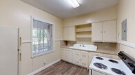 Located at 1528 Wildwood Ave in Columbus, Georgia, this 2-bedroom, 1-bathroom home offers a practical and characterful single-floor layout. The living room serves as the heart of the home, highlighted by a classic white-mantled brick fireplace, crown molding, built-in shelving, a ceiling fan, and warm carpeted flooring — creating a welcoming, traditional atmosphere. Both bedrooms are carpeted and feature ceiling fans and natural light from multiple windows dressed with blinds. The primary bedroom includes crown molding and a built-in shelved closet, adding both charm and functional storage. The bathroom is appointed with classic black-and-white mosaic tile flooring, a pedestal sink, a large mirror, and a full soaking tub with shower — a nod to timeless design. The kitchen is equipped with white cabinetry, open shelving, a deep utility-style sink, laminate countertops, a coil-burner range, and a window overlooking greenery outside. Wood-look flooring runs through the kitchen and connecting hallways. A dedicated laundry room with a stacked washer and dryer unit adds everyday convenience. Multiple hallways connect the spaces fluidly throughout the home.